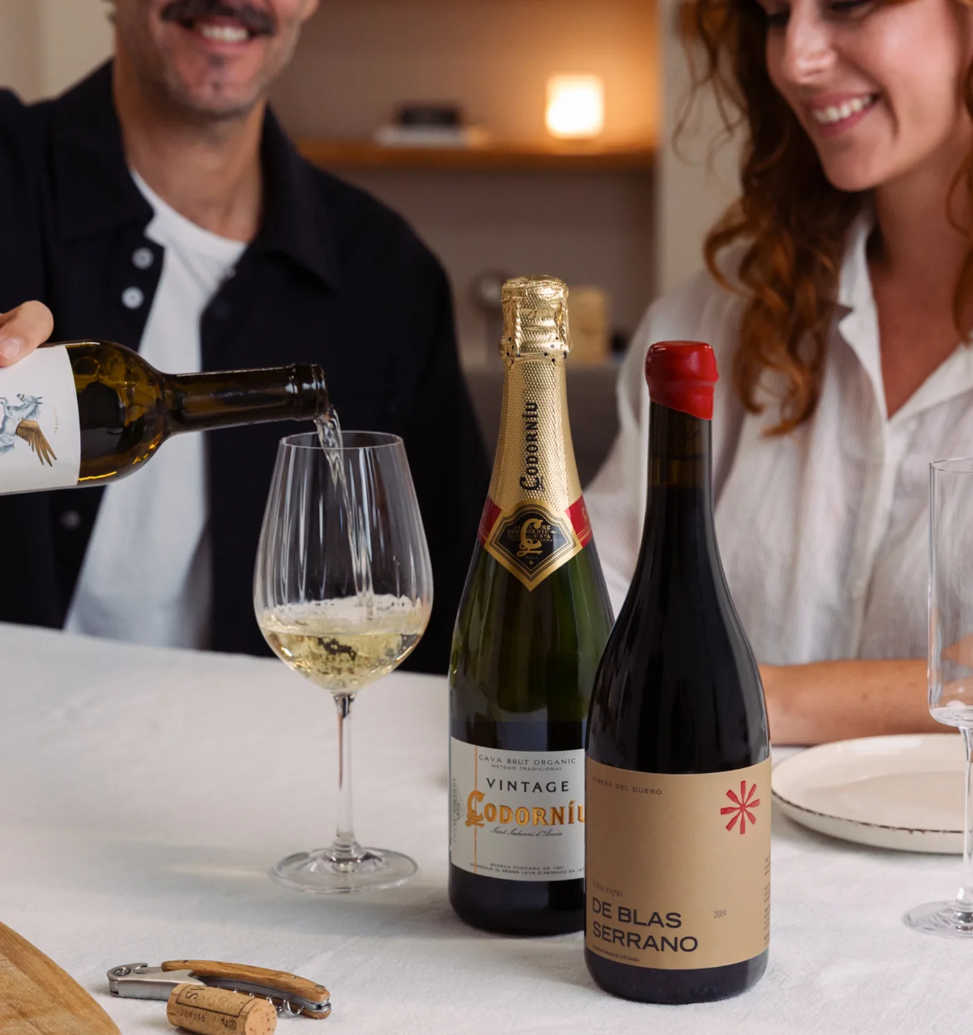 Couple trinquant avec du vin blanc, du cava et du rouge à table